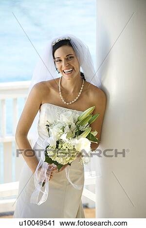 Stock Image - Caucasian mid-adult bride holding bouquet laughing.. Fotosearch