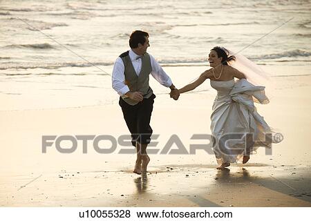 Stock Photo - Caucasian prime adult male groom and female bride running barefoot on beach.. Fotosearch