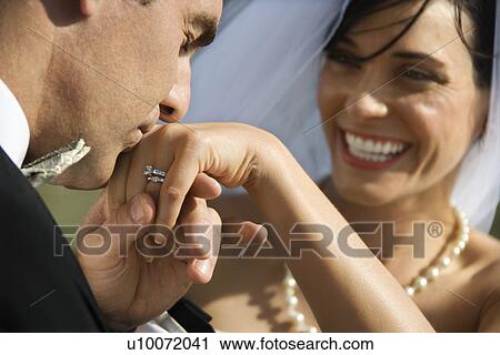 Stock Image - Caucasian prime adult male groom kissing hand of female bride.. Fotosearch