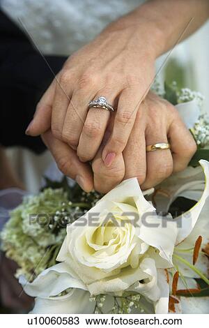 Stock Image - Close up image of bride and groom's hands overlapping.. Fotosearch