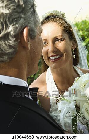 Stock Image - Looking over groom's shoulder at smiling bride.. Fotosearch