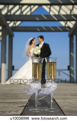 Pair of flute glasses of champagne with Caucasian bride and groom blurred in background. View Large Photo Image Stock Photograph - Pair of flute glasses of champagne with Caucasian bride and groom blurred in background.. Fotosearch