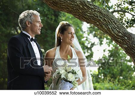Stock Image - Portrait of bride and groom holding hands outside.. Fotosearch