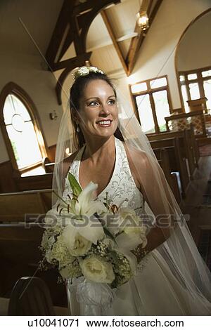 Stock Image - Portrait of mid-adult bride holding bouquet leaving a church. . Fotosearch