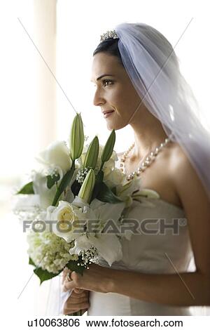 Stock Photograph - Profile portrait of Caucasian mid-adult bride holding flower bouquet.. Fotosearch