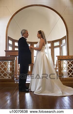 Stock Photo - Protrait of bride and groom holding hands at the alter of a church.. Fotosearch