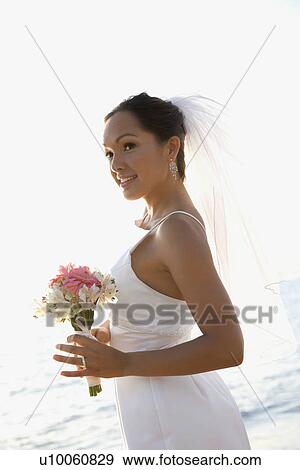 Young adult female Caucasian bride holding bouquet on beach. View Large Photo Image Stock Photo - Young adult female Caucasian bride holding bouquet on beach.. Fotosearch