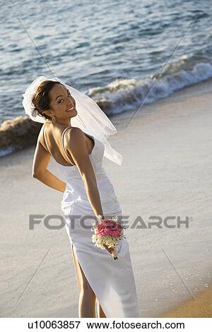 Stock Photo - Young adult female Caucasian bride standing on beach.. Fotosearch