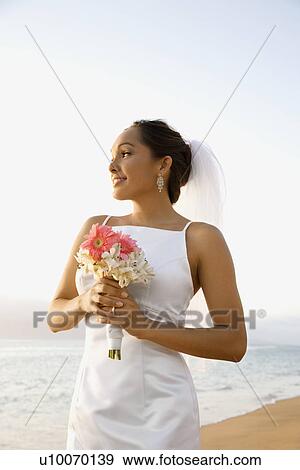 Stock Photo - Young adult female Caucasian bride holding bouquet on beach.. Fotosearch