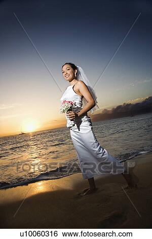 Young adult female Caucasian bride walking holding bouquet on beach. View Large Photo Image Stock Photograph - Young adult female Caucasian bride walking holding bouquet on beach.. Fotosearch