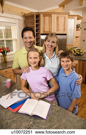 Stock Image - Caucasian family of four standing in kitchen posing with homework on counter.. Fotosearch