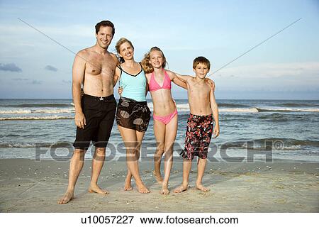 Stock Photo - Caucasian family of four standing on beach.. Fotosearch