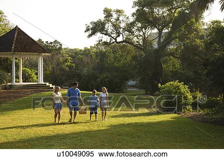 Stock Photography - Caucasian family of four walking in park carrying picnic basket.. Fotosearch