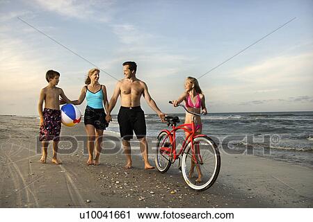 Stock Image - Caucasian family of four walking on beach.. Fotosearch