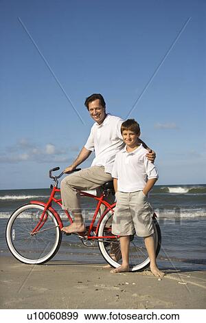 Stock Photo - Caucasian father and pre-teen boy standing on beach with bicycle.. Fotosearch
