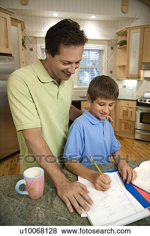 Stock Photo - Caucasian mid-adult father helping pre-teen son with homework in kitchen.. Fotosearch