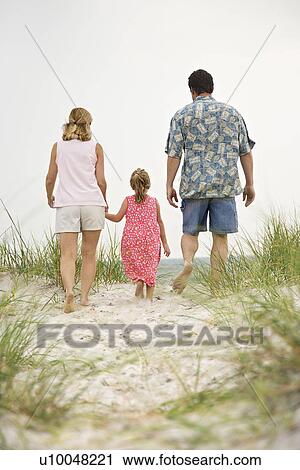 Stock Image - Caucasian mid-adult man and woman walking with female child toward beach.. Fotosearch