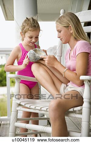 Stock Photo - Caucasian pre-teen girl showing conch shell to other Caucasian female child.. Fotosearch