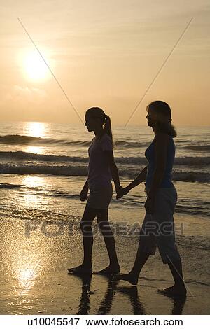 Caucasian prime adult female and female child walking on beach at sunset holding hands. View Large Photo Image Stock Photo - Caucasian prime adult female and female child walking on beach at sunset holding hands.. Fotosearch