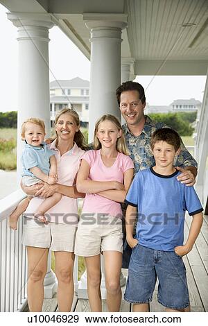 Stock Photo - Family portrait of Caucasian mid-adult man and woman with pre-teen girl and boy and male toddler, standing on porch.. Fotosearch