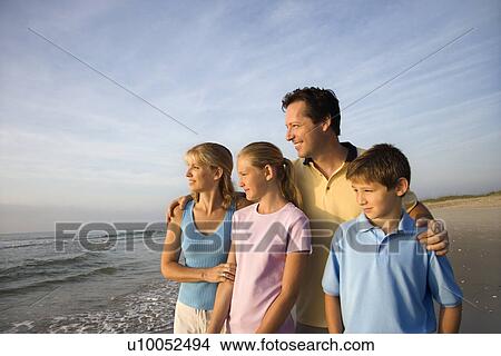 Portrait of Caucasian family of four posing on beach looking at ocean. View Large Photo Image Picture - Portrait of Caucasian family of four posing on beach looking at ocean.. Fotosearch