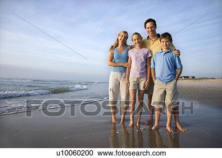 Stock Image - Portrait of Caucasian family of four posing on beach looking at viewer smiling.. Fotosearch
