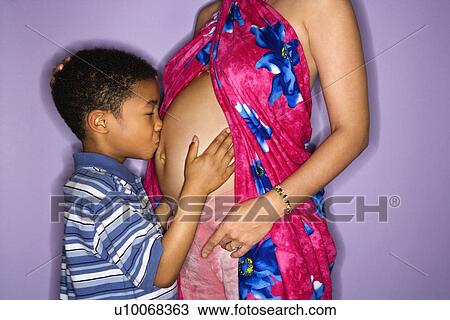 Stock Image - Portrait of expecting female with son kissing stomach.. Fotosearch