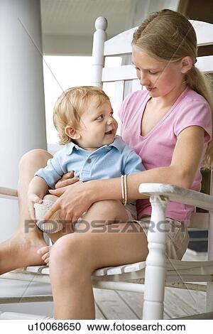 Stock Image - Pre-teen girl holding a toddler looking at each other. Fotosearch