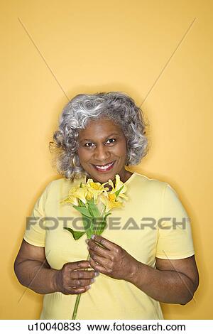 Stock Image - African American female mature adult holding flowers looking at viewer smiling.. Fotosearch