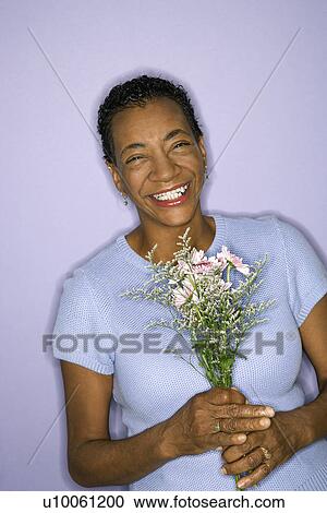 Stock Image - African American mature adult female holding flowers.. Fotosearch