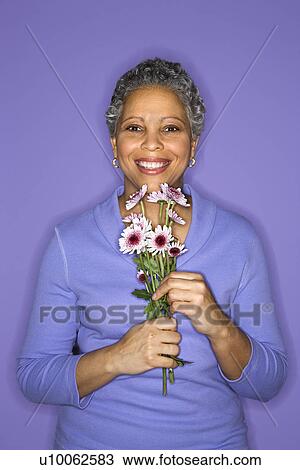 Stock Image - African American mature adult female holding flowers.. Fotosearch