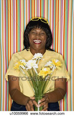 Stock Photograph - African-American mid-adult woman laughing holding flowers.. Fotosearch