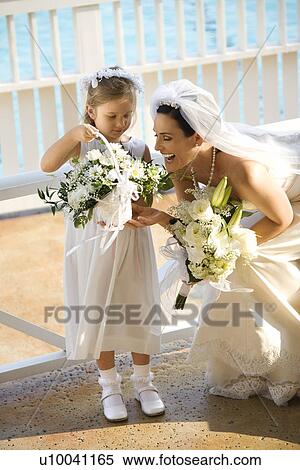 Stock Photography - Caucasian mid-adult bride kneeling next to flower girl admiring her flowers.. Fotosearch