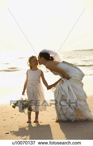 Caucasian mid-adult bride kneeling to give flower girl a kiss on the cheek while holding hands barefoot on beach. View Large Photo Image Stock Photo - Caucasian mid-adult bride kneeling to give flower girl a kiss on the cheek while holding hands barefoot on beach.. Fotosearch