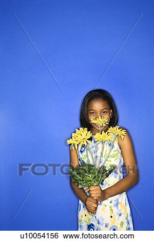 Stock Photograph - Portrait of African-American teen girl holding a bouquet of daisies in front of blue background.. Fotosearch