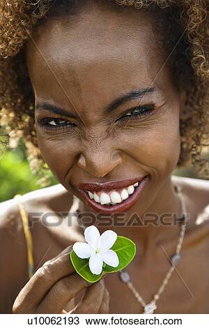 Stock Image - Portrait of mid-adult Black female squinting and holding jasmine flower.. Fotosearch