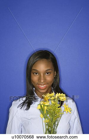 Stock Photo - Portrait of smiling African-American teen girl with bouquet of yellow flowers in front of blue background.. Fotosearch