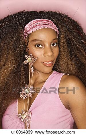 Stock Photo - Portrait of smiling young African-American adult woman with big hair on pink background holding glass bead flowers.. Fotosearch