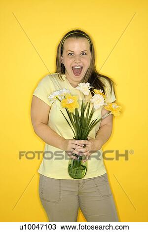 Stock Image - Young adult female Caucasian standing holding flowers.. Fotosearch