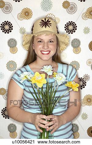 Stock Image - Young Caucasian woman wearing straw hat holding flower bouquet.. Fotosearch