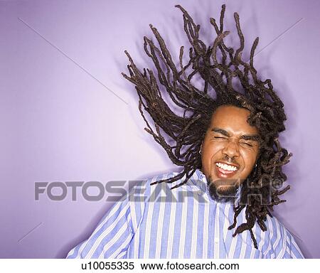 Stock Photography - African-American mid-adult man on purple background with his dreadlocks in motion.. Fotosearch