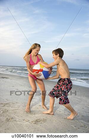 Stock Image - Caucasian pre-teen boy and girl pulling on beachball.. Fotosearch