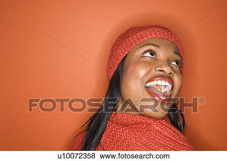 Stock Photo - Laughing African-American mid-adult woman wearing orange scarf and hat on orange background.. Fotosearch