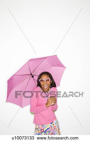 Stock Image - Portrait of African-American teen girl holding a pink umbrella standing in front of white background.. Fotosearch