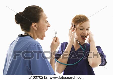 Stock Image - Portrait of Caucasian healthcare workers wearing scrubs with one yelling into stethoscope that is attached to other's ears against white background.. Fotosearch