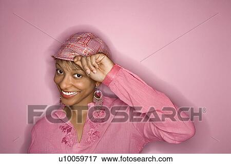 Portrait of smiling African- American young adult woman on pink background tipping her hat. View Large Photo Image Stock Photo - Portrait of smiling African- American young adult woman on pink background tipping her hat.. Fotosearch