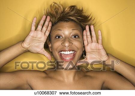 Stock Photo - Portrait of young African-American adult woman on yellow background yelling at the viewer.. Fotosearch