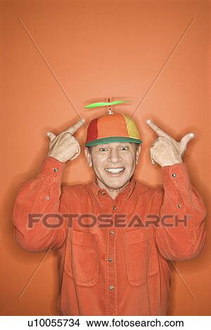Picture - Smiling middle-aged Caucasian man wearing propeller cap on orange background.. Fotosearch
