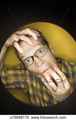 Stock Image - Vignette of adult Caucasian man on yellow background pulling at face and looking stressed out.. Fotosearch