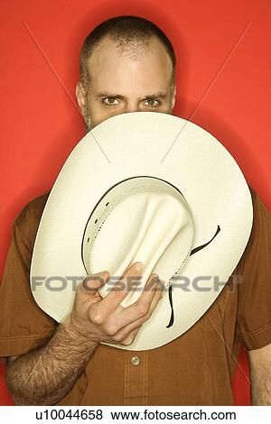 Caucasian man peering over cowboy hat partially covering his face against orange background. View Large Photo Image Stock Photo - Caucasian man peering over cowboy hat partially covering his face against orange background.. Fotosearch